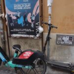 Electric scooter and bicycle parked by poster