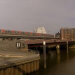 Train on bridge over canal in Hamburg cityscape with modern architecture.