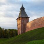 Historic Kremlin tower in Veliky Novgorod, Russia at sunset, surrounded by greenery and bright skies.