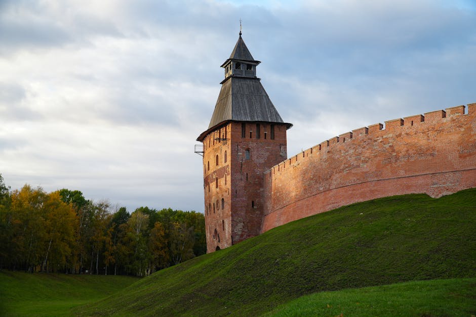 Historic Kremlin tower in Veliky Novgorod, Russia at sunset, surrounded by greenery and bright skies.