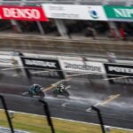 Motorcycles racing on a wet track during a race.