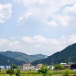 white and brown concrete building near green mountain under white clouds during daytime