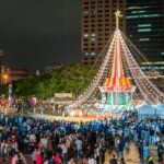Crowd gathered around a large illuminated christmas tree at night.